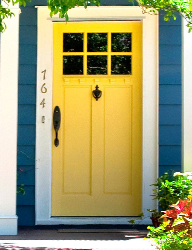 Blue house exterior with yellow door, new windows, flowers, plants, and covered porch area.